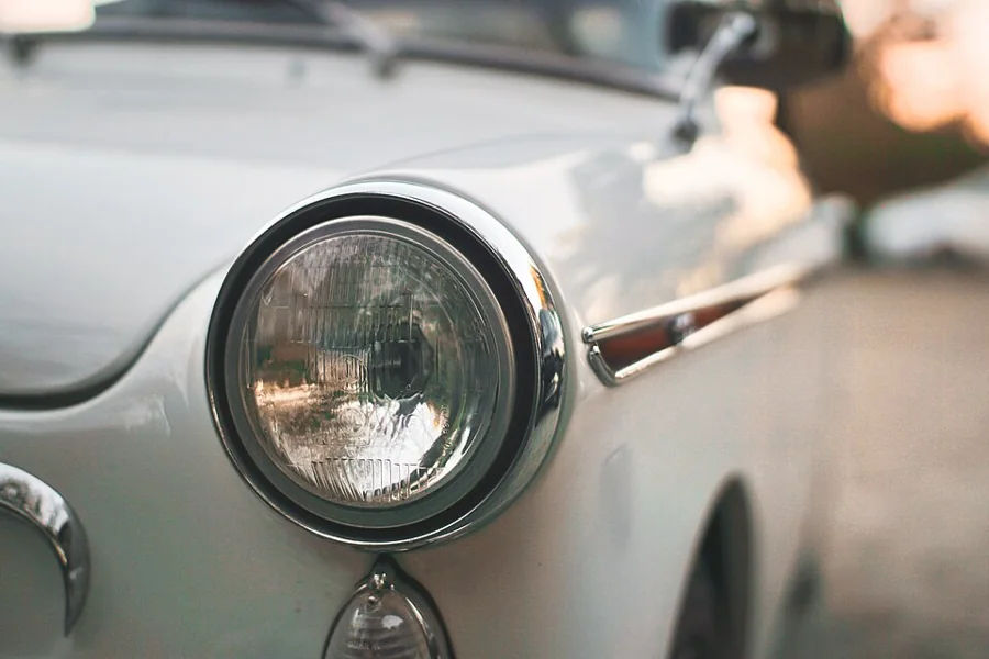 Chrome-trimmed round headlight of a white car
